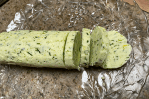 Garlic Scape and Chive Compound Butter in log with some slices on glass plate