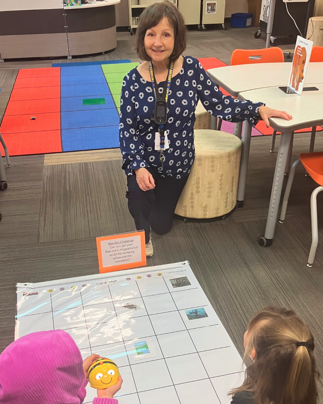 Janet Vraney kneeling in school classroom working with two students
