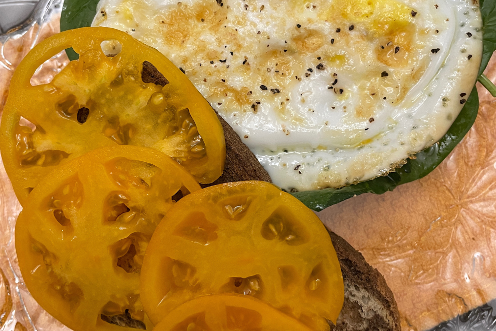 2 pieces of marbled rye bread, one piece has sliced golden heirloom tomatoes, the other piece has spinach with fried duck duck on top