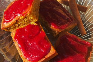 Four pumpkin bar squares with cranberry sauce spread on each displayed on a glass plate