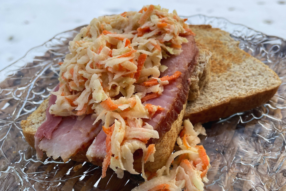 RabiSlaw made with grated carrots, cabbage, kohlrabi, and seeds served over ham and toast