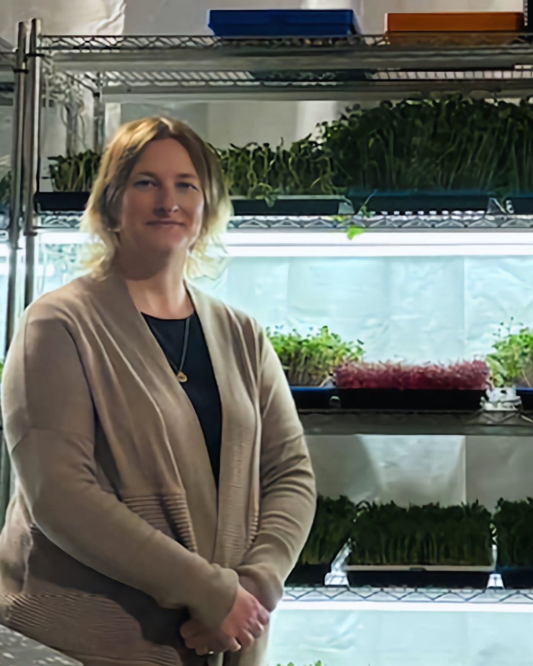 Mary Fox standing in front of shelves with trays of microgreens