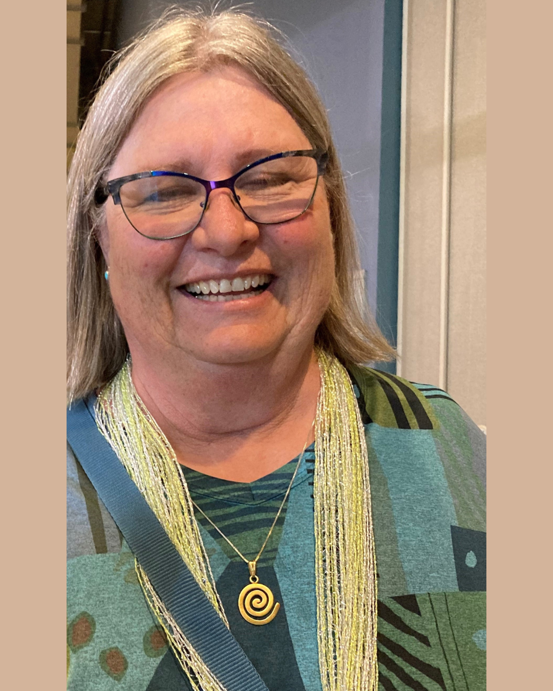 Val Dantoin smiling in blue and green patterned shirt and green scarf
