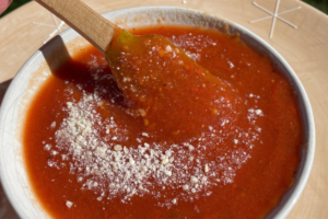 Pizza sauce in white bowl with spatula dipped in bowl, topped with shredded parm