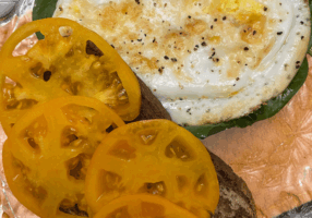 2 pieces of marbled rye bread, one piece has sliced golden heirloom tomatoes, the other piece has spinach with fried duck duck on top