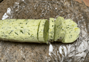 Garlic Scape and Chive Compound Butter in log with some slices on glass plate