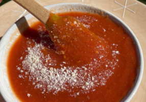 Pizza sauce in white bowl with spatula dipped in bowl, topped with shredded parm