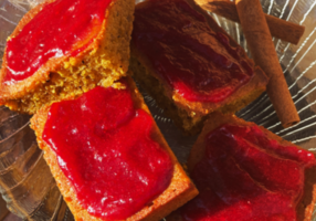Four pumpkin bar squares with cranberry sauce spread on each displayed on a glass plate